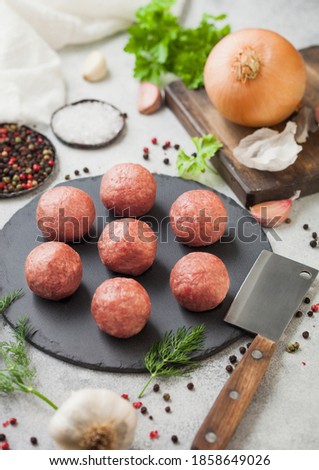 Fresh beef raw meatballs on stone board with pepper, salt and garlic on light table background with dill,parsley and dill. Top view
