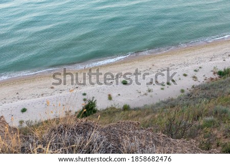 View from cliff edge on sea shore with white sand blue water and dry grass