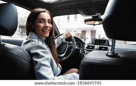 Elegant woman driver looking at backseat, smiling happy, asking passanger fasten seatbelt. Businesswoman talking to person in her car, driving at work. Royalty-Free Stock Photo #1858695745