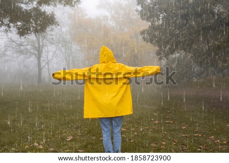 Carefree woman in raincoat having fun while running on a rainy day. stock photo