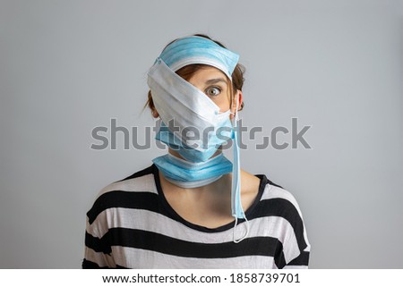 Funny portrait of a overprotective woman with whole face covered in surgical masks in a gray background