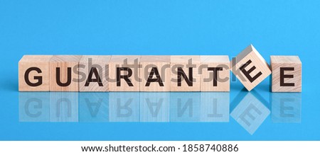 Text GUARANTEE on wood cube block, stock investment concept. The text GUARANTEE is written on the cubes in black letters, the cubes are located on a blue glass surface Royalty-Free Stock Photo #1858740886