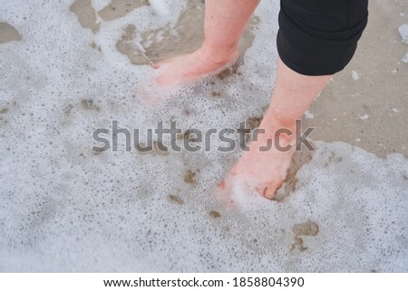 female bare feet stand in the water closeup top view