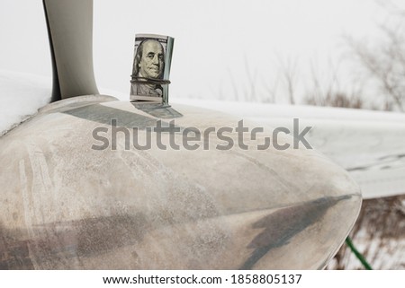 A dollar, a bundle of rolled-up dollars is on the prop of a private plane.