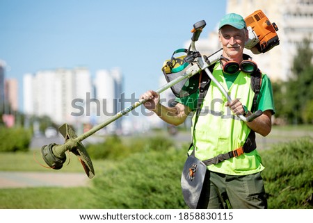 Municipal gardener landscaper senior man worker with gas grass trimmer equipment on sunlight city background Royalty-Free Stock Photo #1858830115