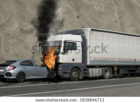 Collision between a car and a truck transporting goods. Accident followed by fire. The car caught fire after the frontal impact. Royalty-Free Stock Photo #1858846711