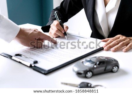 Closeup of Asian female signing car insurance document or lease paper contract or agreement. Buying or selling new or used vehicle with car keys on table. Royalty-Free Stock Photo #1858848811