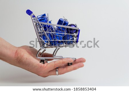 Man hand holding small shopping cart with blue gift on white backgorund. Merry christmas sale, copy space