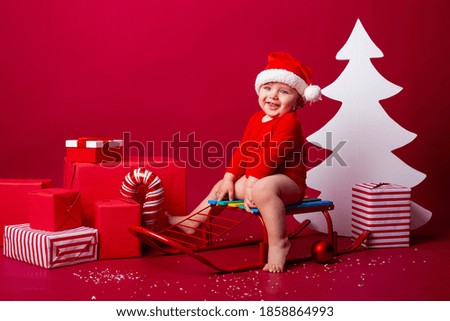 Cute baby Santa sits on a sled with Christmas gifts. Christmas concept, text space