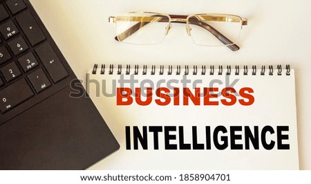 Business analytics text written on a notebook, next to a laptop and glasses on a white background