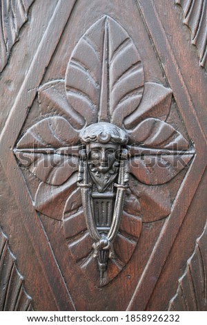 Detail of an old door knocker with an human head on a carved wood door in Lucca, Italy. High quality photo