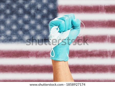Doctor fist hand in protective glove holding a mask in front of flag of the United States of America. Concept of stop covid-19 disease.