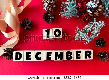 December 10 on wooden cubes.Near fir branches, cones, ribbon, gift box on a red background.Calendar for December.