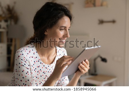 Smiling young Caucasian woman look at tablet screen browse surf wireless internet on gadget. Happy millennial female use pad device, watch webinar or video online. Communication concept.