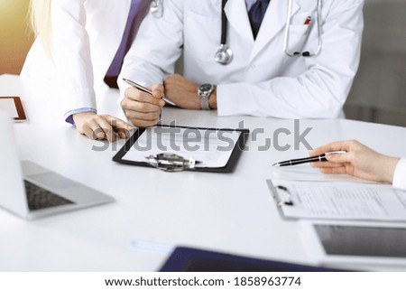 Group of unknown doctors are sitting at the desk and discussing problems or disease treatment in sunny hospital office. Covid 2019