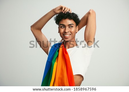 Man with a lgbtq flag on his shoulder looking away. Gay man in crop top posing on white background.