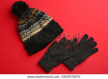 Woolen gloves and hat on red background, flat lay