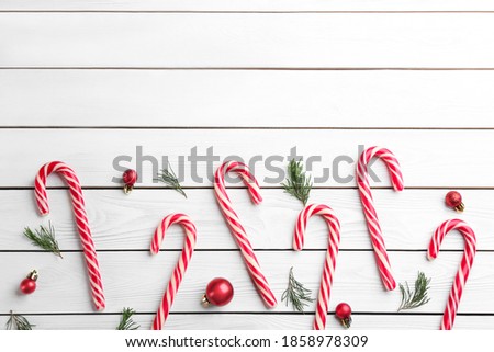 Candy canes, fir branches and Christmas balls on white wooden table, flat lay. Space for text