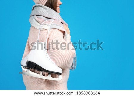 Happy woman with ice skates on light blue background, closeup. Space for text