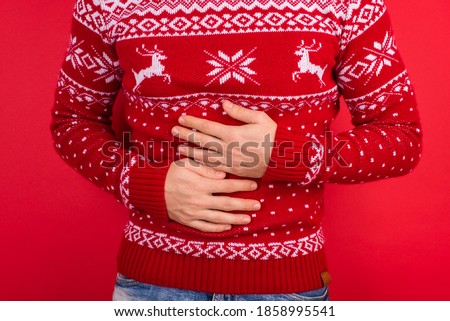 Bellyache concept. Close up photo of men in red winter sweater with deers holding his stomach isolated on red background