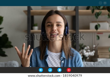 Head shot beautiful young caucasian woman in headphones sitting on sofa, involves in online video call conversation, working or study distantly alone from home, laptop application screen view. Royalty-Free Stock Photo #1859040979