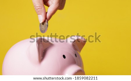 Hand putting money into Piggy bank on yellow background for economy, saving money wealth and financial concept Royalty-Free Stock Photo #1859082211