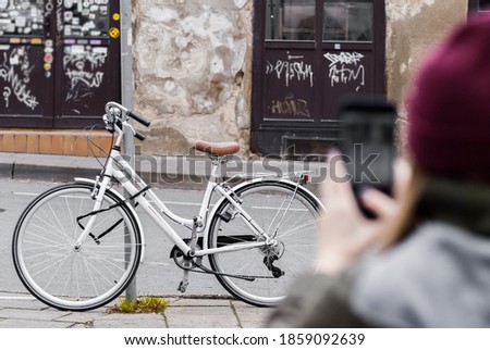 Girl taking photo of vintage bicycle using the phone. White retro bicycle locked to a pipe on an old street.