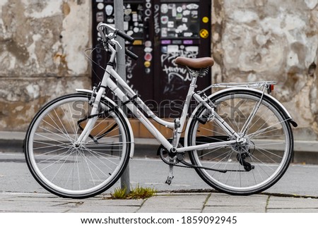 White vintage bicycle parked on the street. Bike locked to the metal pipe. Royalty-Free Stock Photo #1859092945