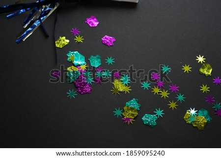 Scattered mixed shiny festive confetti decorations on a black background. Surprise. Multicolored gift boxes. Stars. Festivity. New Year. Christmas. Winter holidays. Top view.