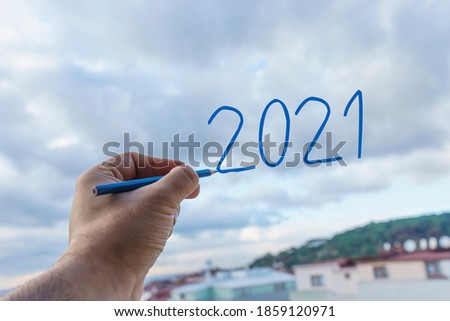 New Year 2021 is coming concept.  
Hand writing 2021 with blue pen in the sky.