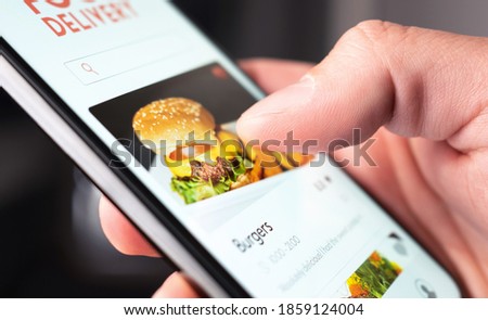 Food delivery app order with phone. Online mobile service for take away burger and pizza. Hungry man reading restaurant menu, website and reviews with smartphone. Takeout or fast courier deliver. Royalty-Free Stock Photo #1859124004