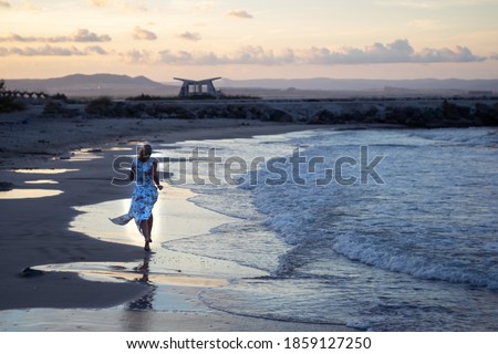 girl walking along the beach. Girl in white long summer dress on vacation. Girl on the shore of the ocean. Island. Caucasian woman walks along beautiful seashore