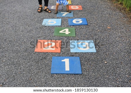 Colourful hopscotch playground markings numbers on stone at pavement with people playing.