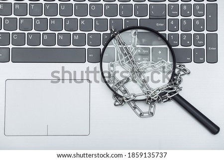 Magnifying glass wrapped in a steel chain on laptop keyboard