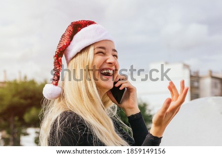Stock photo of a pretty blonde girl talking with friend via mobile phone for Christmas day. She is laughing and having a good time. Happy Christmas, holidays and people concept