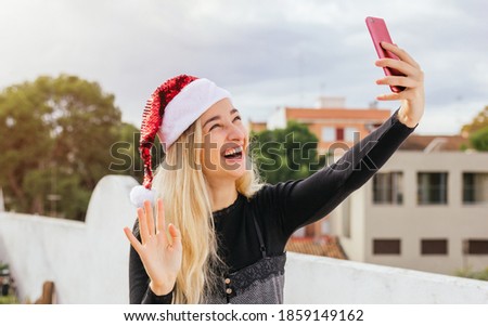 Stock photo of a pretty girl vlogging with mobile phone for Christmas day. She is greeting, laughing and having a good time. Xmas selfie, technology, social networks and people concepts