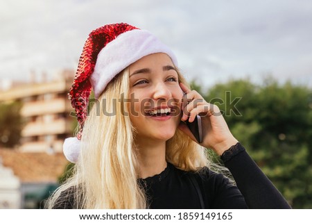 Stock photo of a happy young blonde woman calling on smartphone for Christmas day. She is talking and smiling. Happy Xmas, people and technology concept