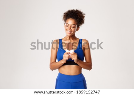 Woman holding tasty chocolate bar and looking at candy with temptation, standing in fitness costume, standing over white background