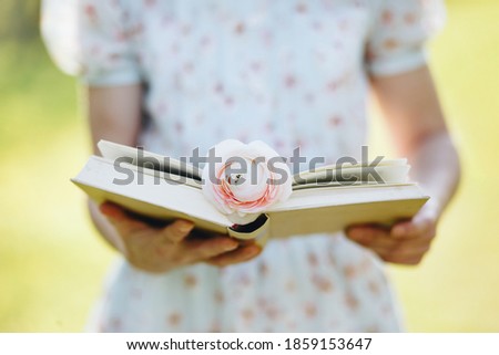 Close-up of female hands holding open book in spring park. Reading concept background