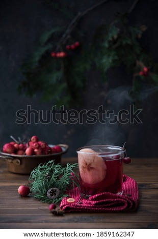glass with mulled wine, steam and festive decor. dark wooden table