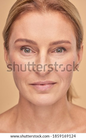 Close up of beautiful mature woman looking at camera isolated over beige background in studio, vertical shot
