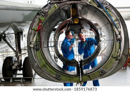 Engineers in uniforms inspecting the engine casing of a passenger jet at a hangar. Royalty-Free Stock Photo #1859176873