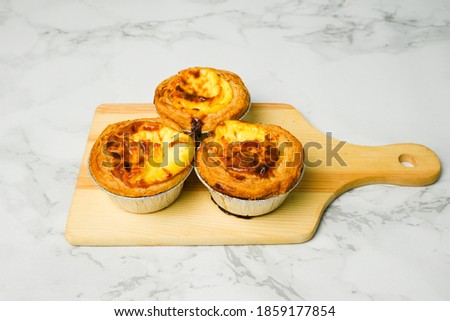 A picture of three famous freshly baked egg tart arranged on wooden board at marble table 
