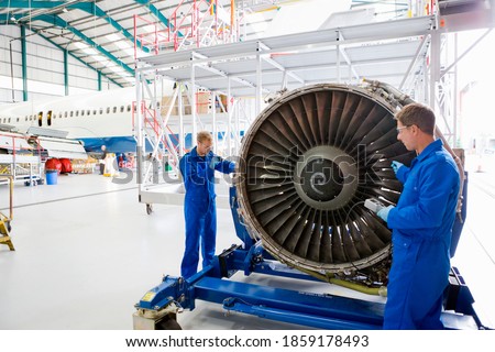 Engineers in uniforms assembling the turbine engine of a passenger jet at a hangar.