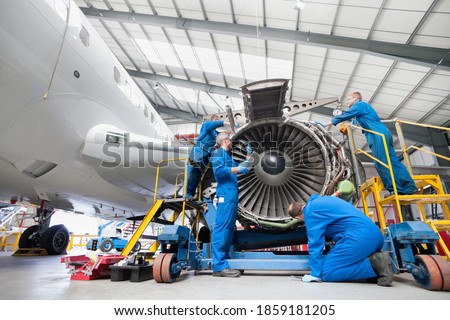 Low-angle wide shot of engineers assembling an engine of a passenger jet at a hangar. Royalty-Free Stock Photo #1859181205