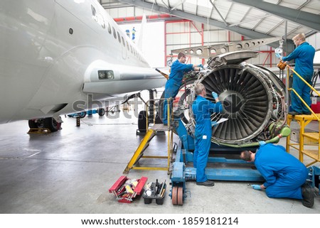 Wide shot of engineers assembling an engine of a passenger jet at a hangar. Royalty-Free Stock Photo #1859181214