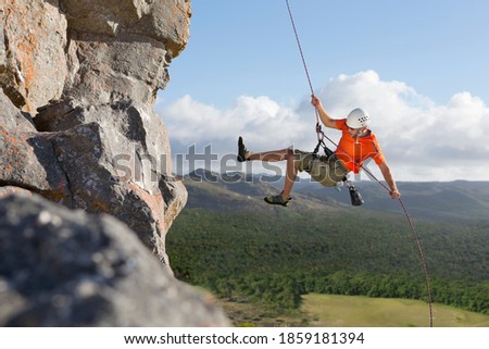 Wide shot of a male rock climber descending down a rock face using a rappelling rope. Royalty-Free Stock Photo #1859181394