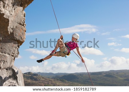 Wide shot of the side view of a female rock climber abseiling down a rock face. Royalty-Free Stock Photo #1859182789