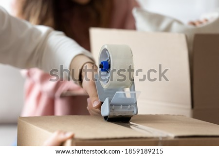 Man holding tape dispenser sealing cardboard box with personal stuff belongings on happy moving day to own house. Family prepare parcel, send cheap services ad, relocation to new apartment concept Royalty-Free Stock Photo #1859189215