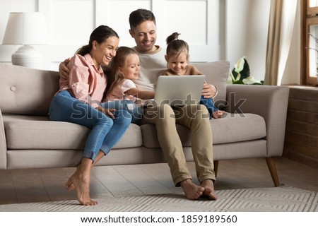 Carefree family with daughters gathered in warm living room relaxing on sofa use laptop watch cartoon comedy movie, educational program for kids, buying online, stay at home at quarantine time concept